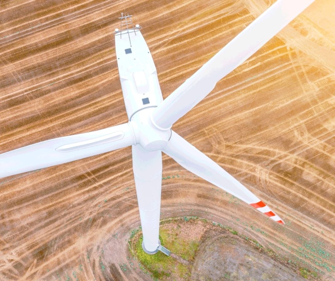 Éolienne vue du dessus dans un champ agricole, avec ses pales blanches et sa tour au centre.